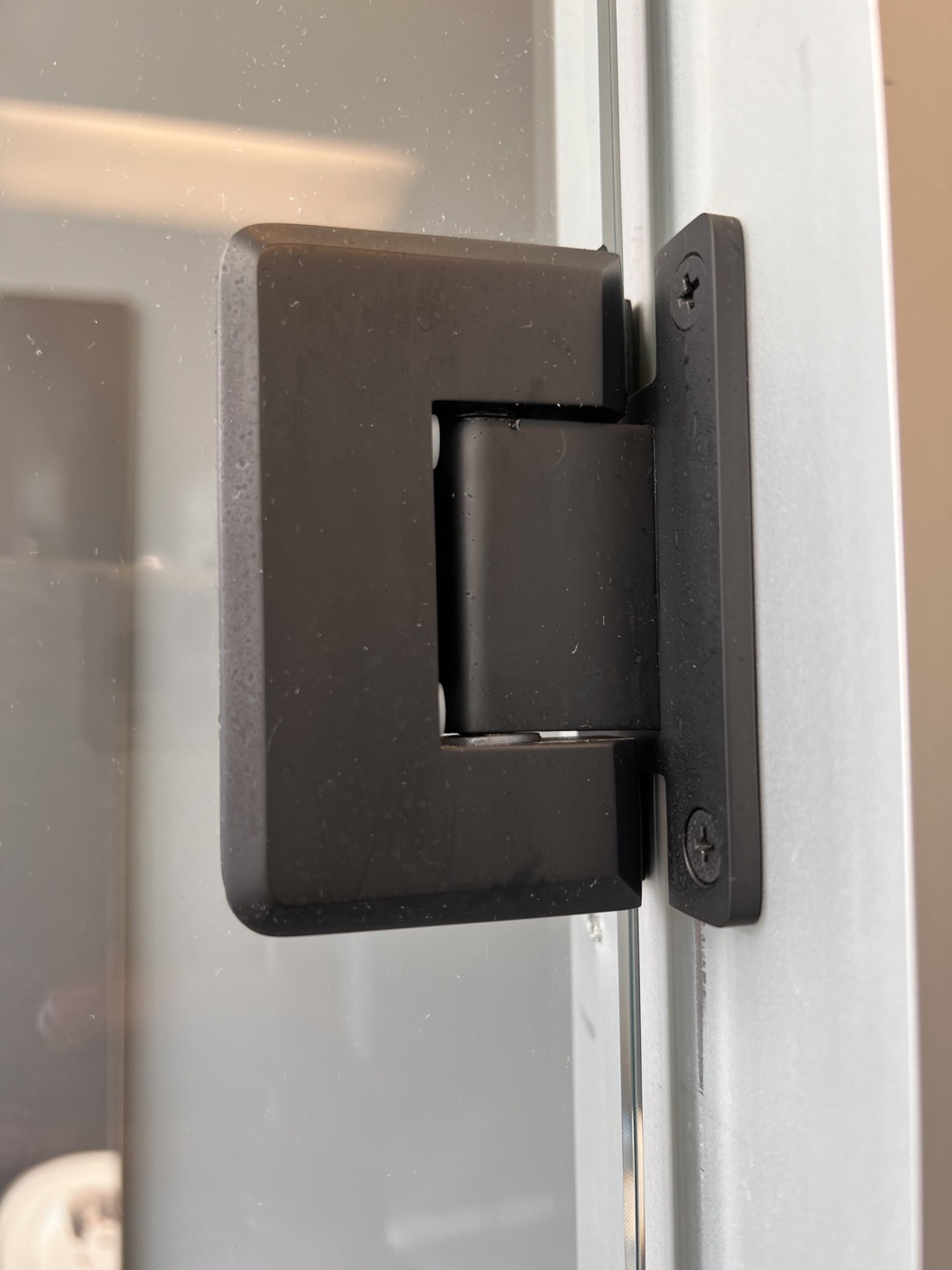 Oil-rubbed bronze shower door hinge and hardware on a frameless glass enclosure