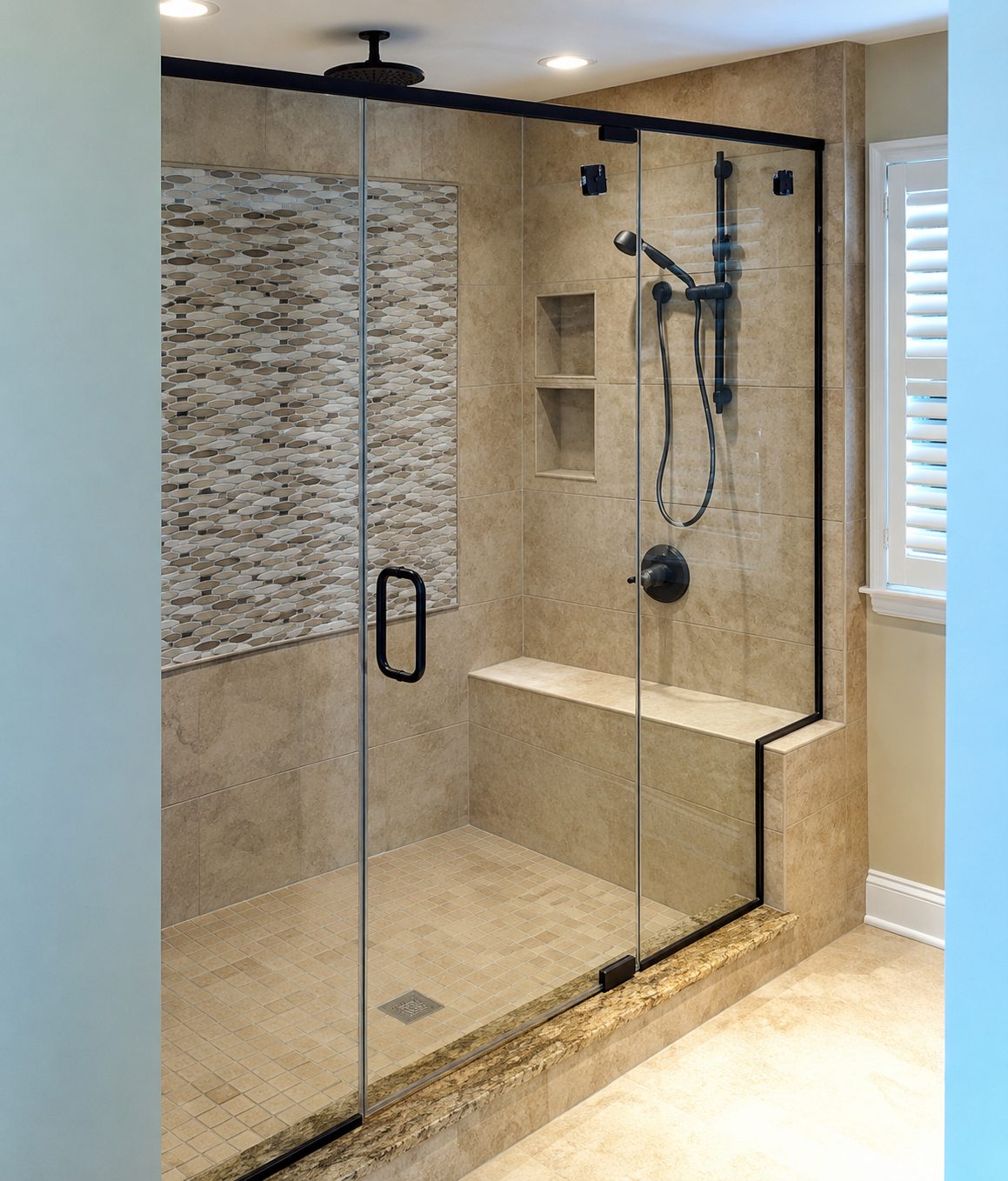 Shower door and fixed panel with a matte black header and channel, oval mosaic accent wall and a tiled bench
