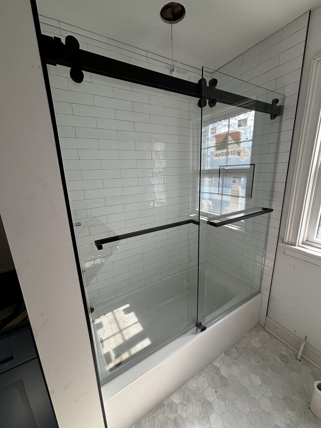 Black-framed sliding tub enclosure over white subway tile