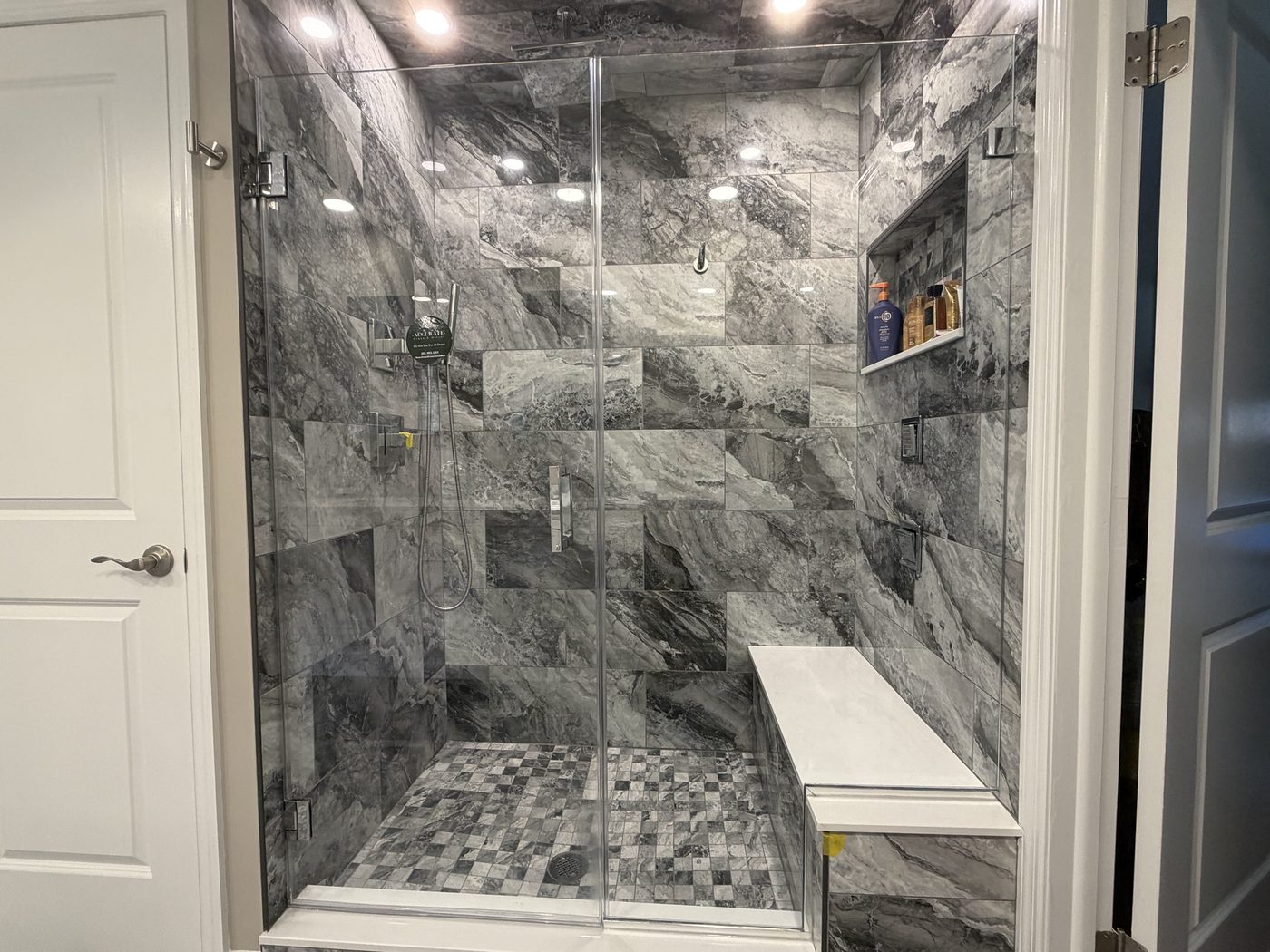 Frameless glass shower with gray marble walls and pebble floor