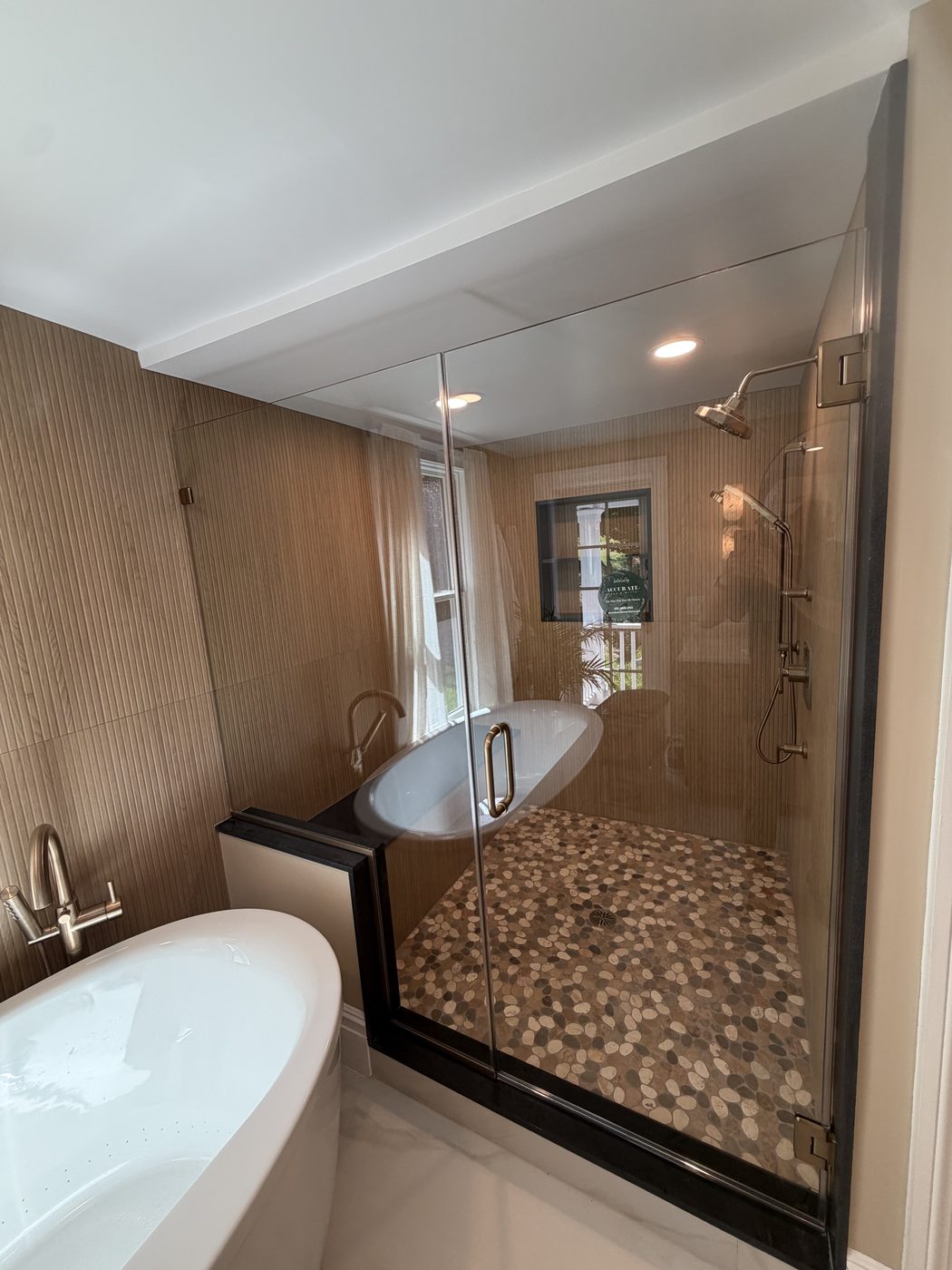 Frameless glass shower beside a freestanding tub with pebble floor